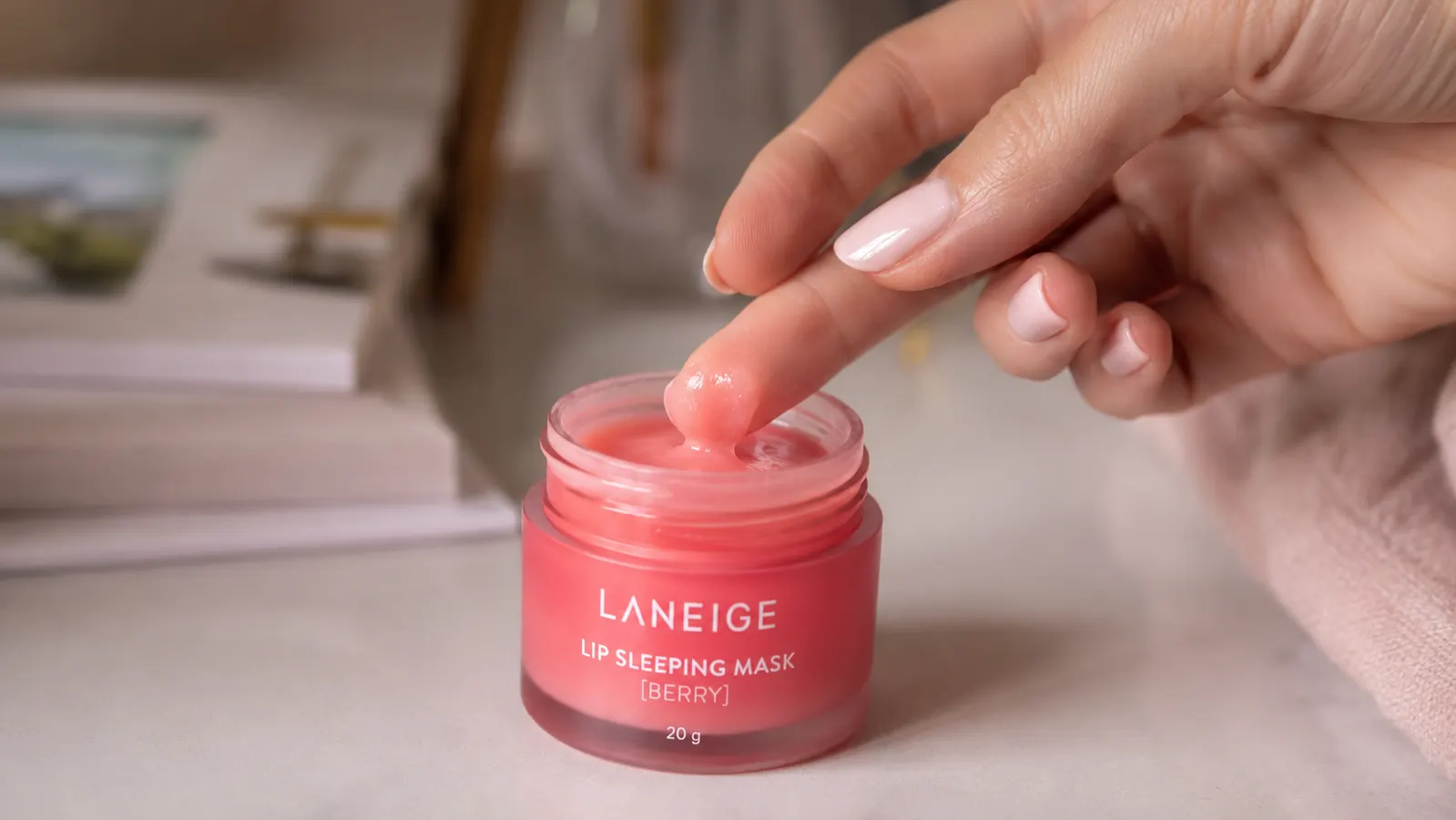 Fingertip dabbing a small amount of lip sleeping mask from the jar onto lips