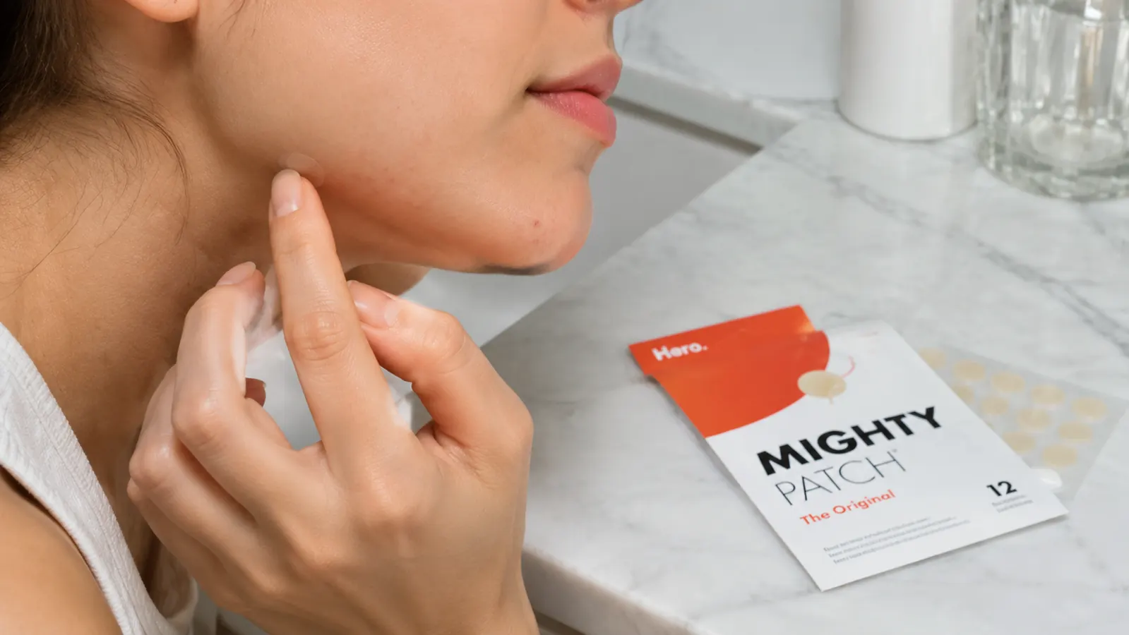 Hand pressing a small clear patch onto a spot near the chin instead of applying cream with a fingertip