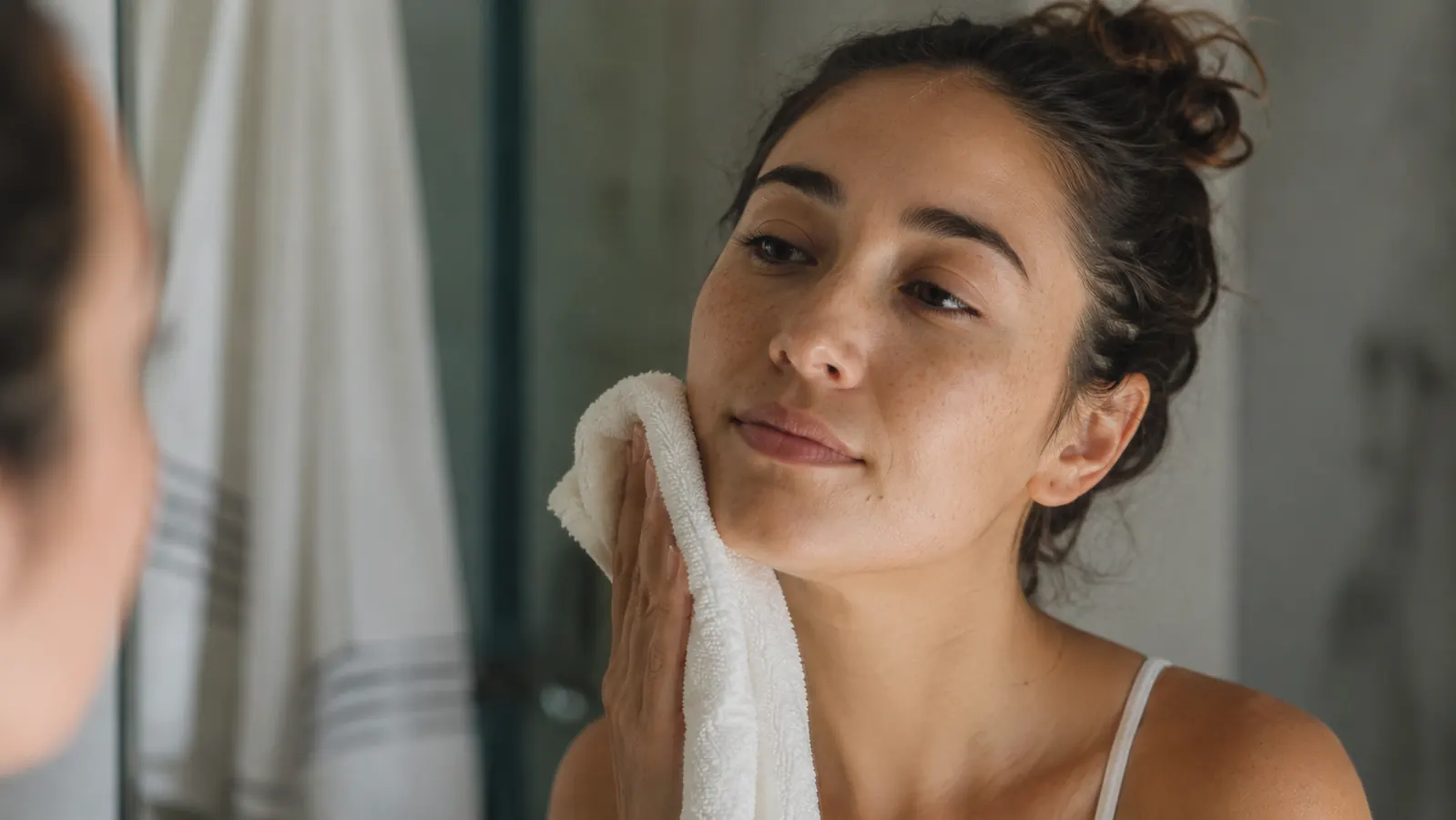 Person patting their face dry with a towel after washing, calm morning bathroom light