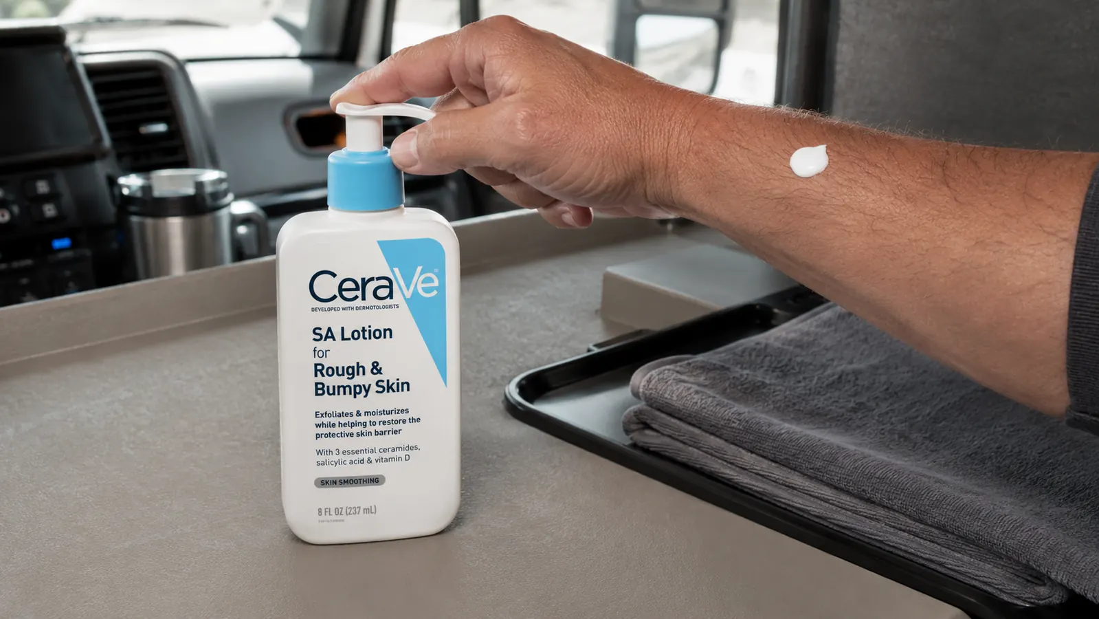 Hand squeezing a small amount of white lotion from the CeraVe SA Lotion pump bottle onto the back of an arm