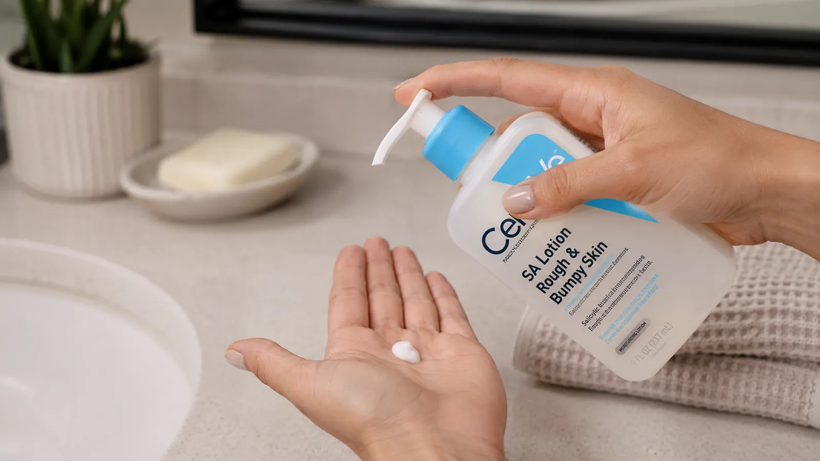 Hand pumping white lotion from a CeraVe SA Lotion bottle onto the palm before applying to the arm
