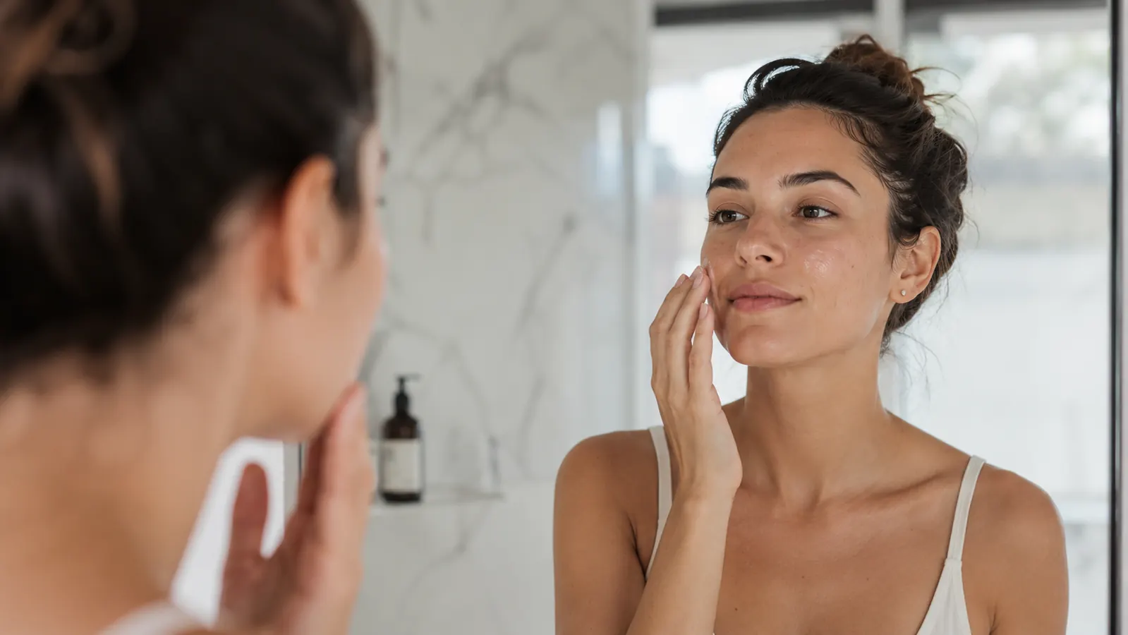 Woman applying a lightweight moisturizer to her cheek after cleansing, still-damp skin
