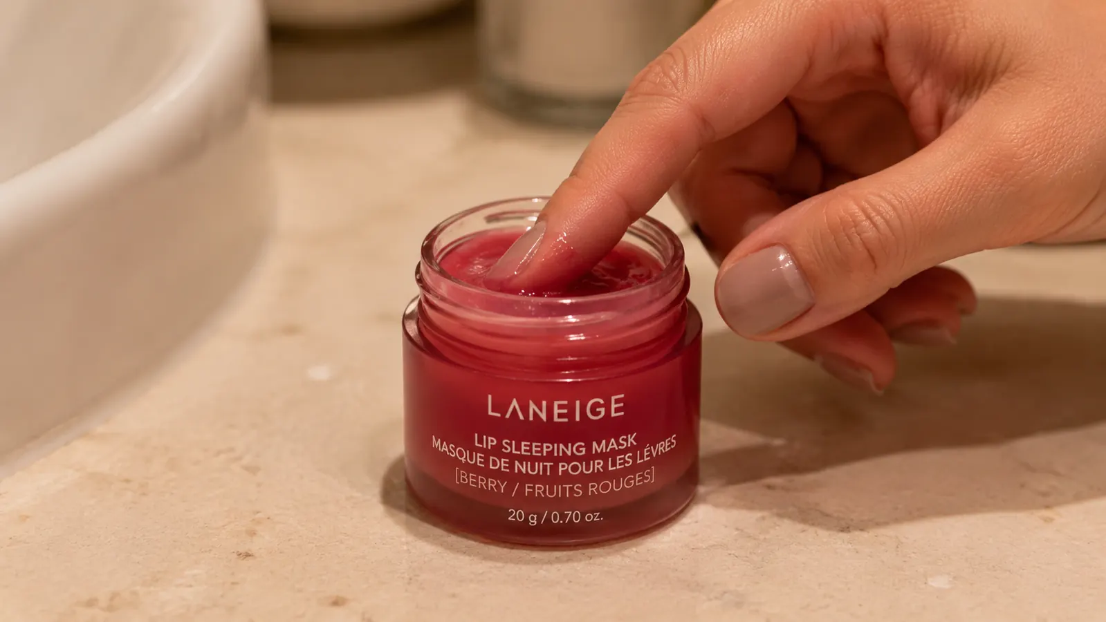 Hand using a fingertip to scoop a small amount of lip sleeping mask from an open jar before bed