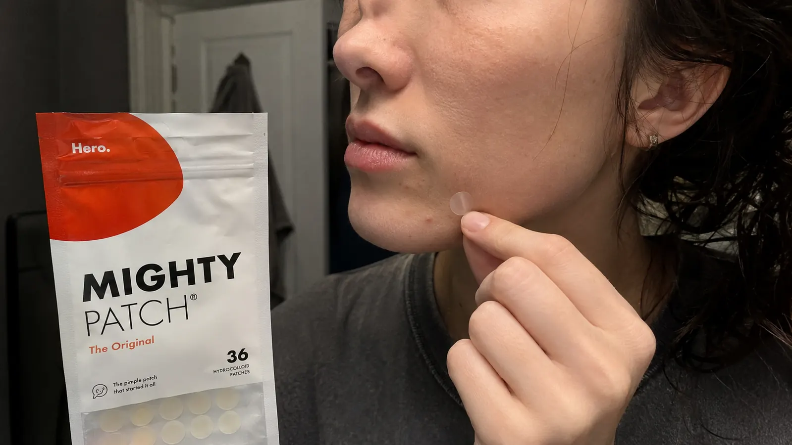 Hand pressing a small round hydrocolloid patch onto a jawline breakout after a night shift