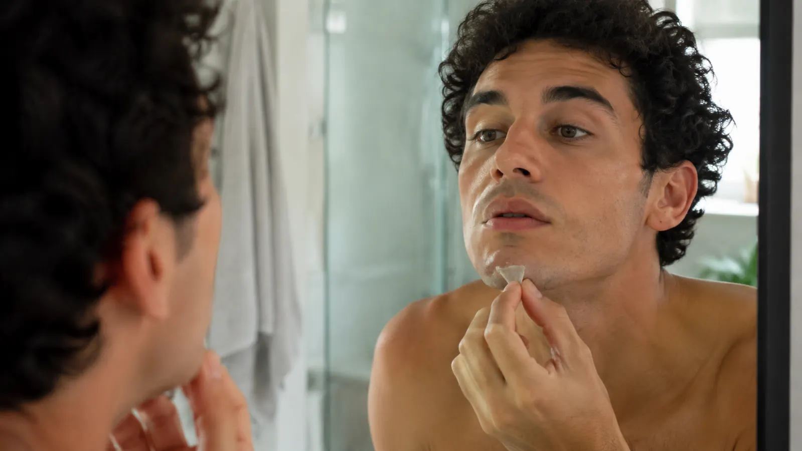 Person peeling a small patch off their chin in daylight while getting ready for the day