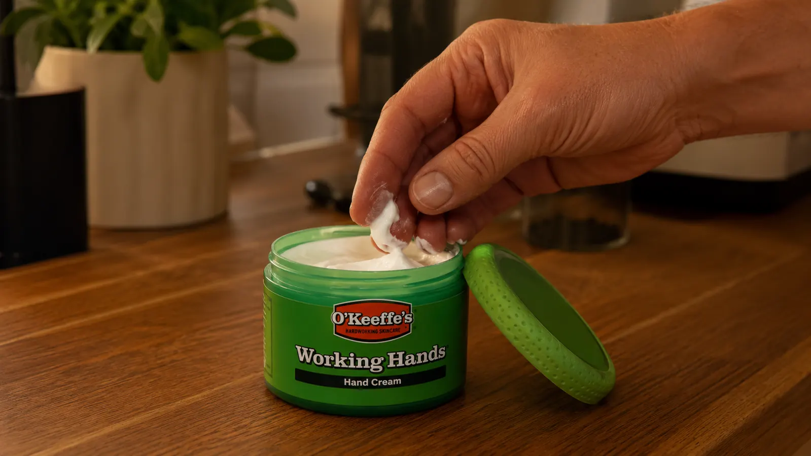 Jar of O'Keeffe's Working Hands hand cream open on a kitchen counter with a fingertip scooping out cream